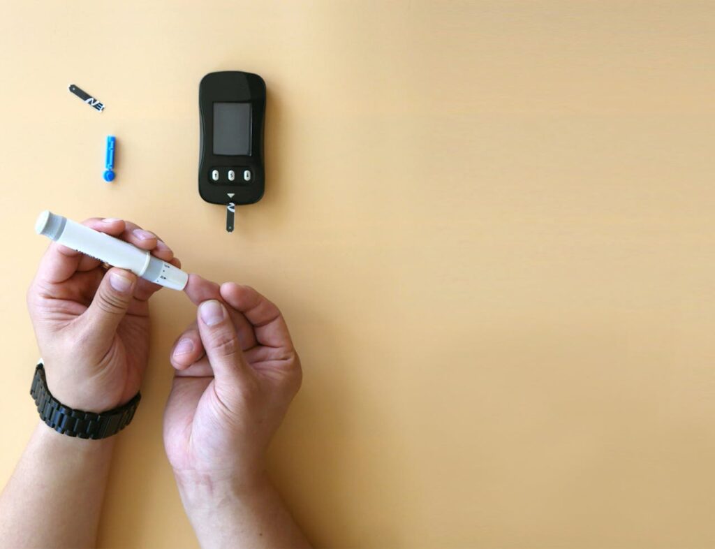 Hands using a glucometer for blood sugar testing on a beige background.
