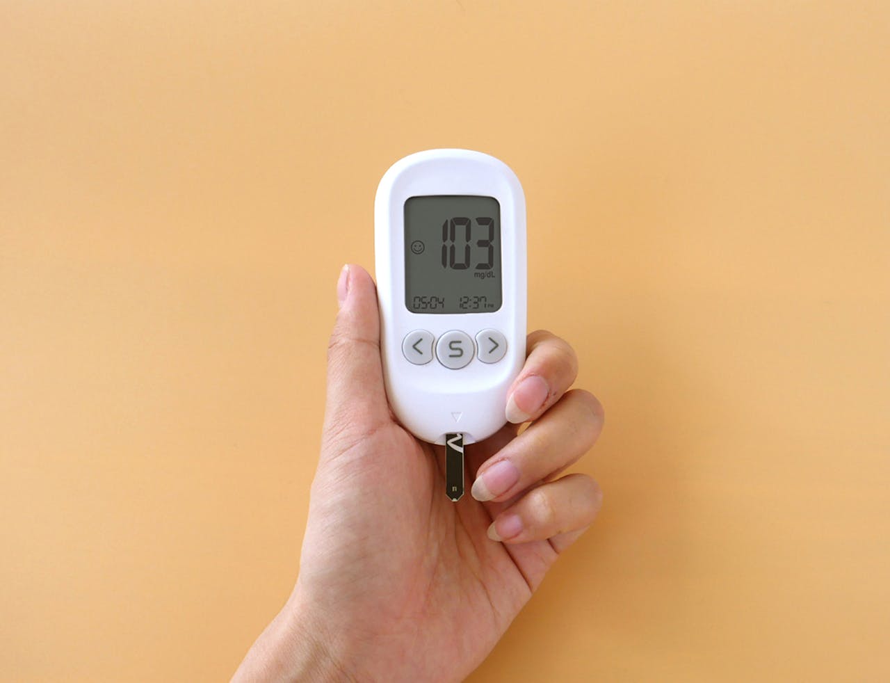 experience-img A hand holding a blood glucose meter displaying 103 mg/dL on a neutral background.